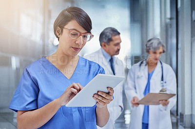 Buy stock photo Cropped shot of a medical practitioner looking at a patient's file on a digital tablet with colleagues in the background