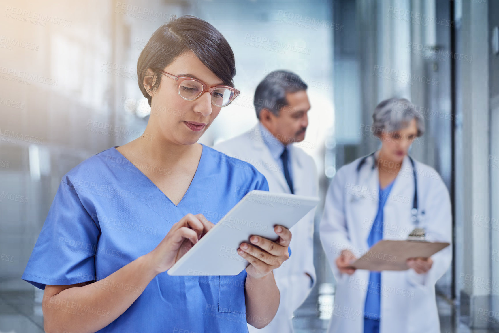 Buy stock photo Woman, doctor and tablet in hospital with scrubs for medical, check on digital file for schedule. Female surgeon, medicine and tech with colleagues in background and working, career in healthcare