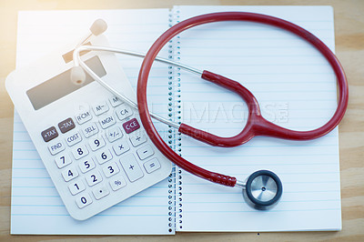 Buy stock photo Closeup shot of a calculator and stethoscope resting on a notebook on a table