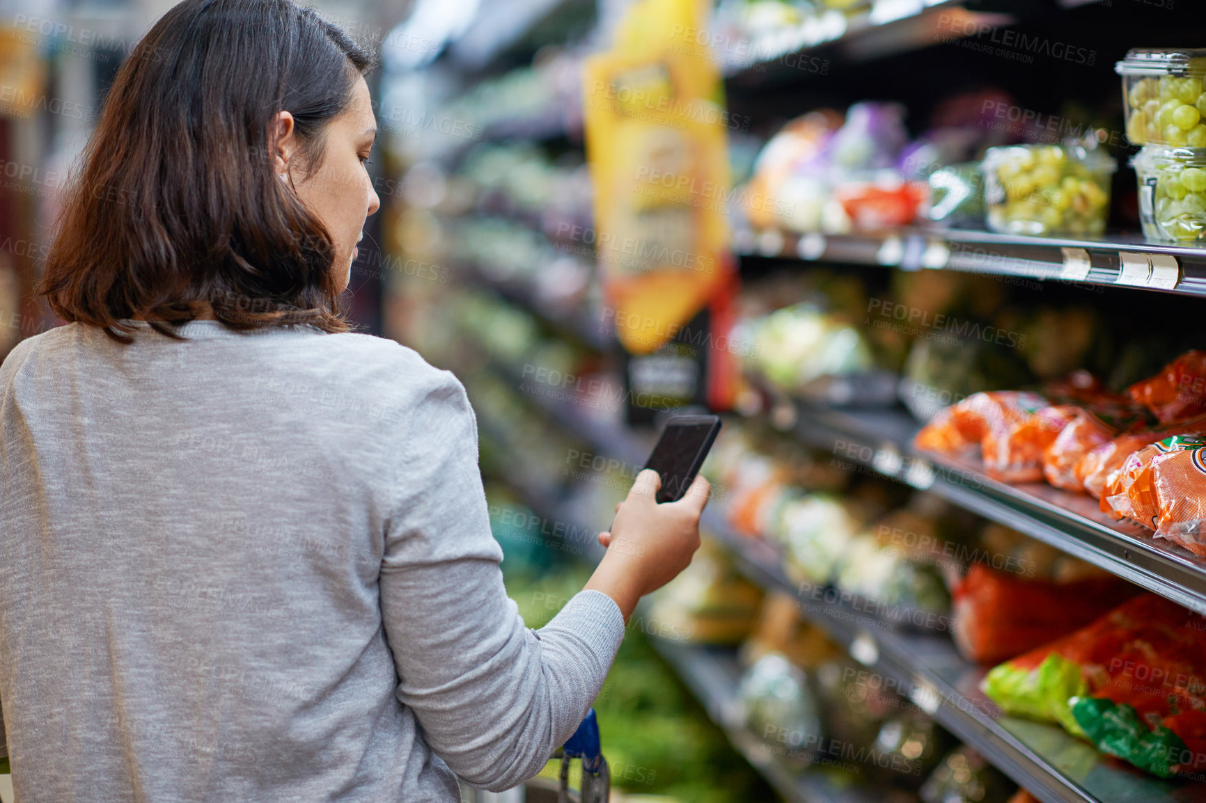 Buy stock photo Cropped shot of a woman checking her digital shopping list on her cellphone in a grocery store