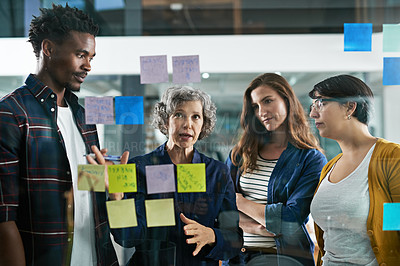 Buy stock photo Shot of a group of colleagues working with adhesive notes on a glass wall in the office