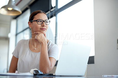 Buy stock photo Shot of a young woman looking through a window while working on a laptop in an office