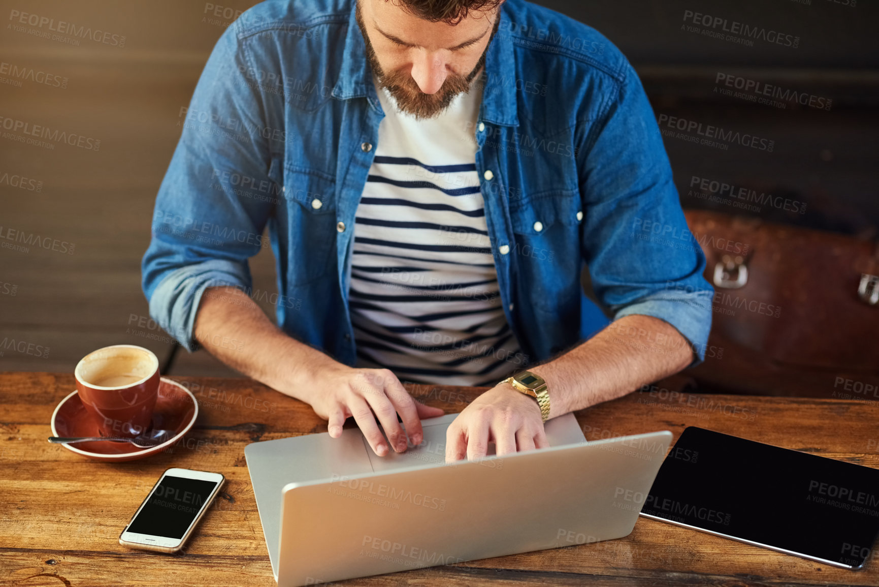 Buy stock photo Cropped shot of a handsome young man working on his laptop in a cafe