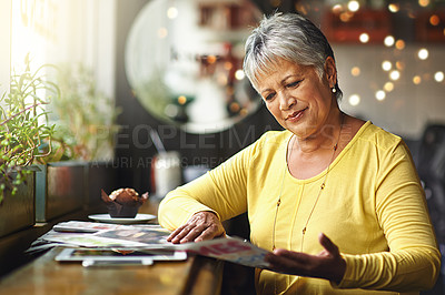 Buy stock photo Shot of a mature woman reading a newspaper in a coffee shop