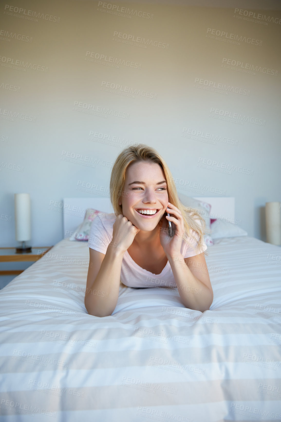 Buy stock photo Shot of a young woman talking on her phone while lying on bed