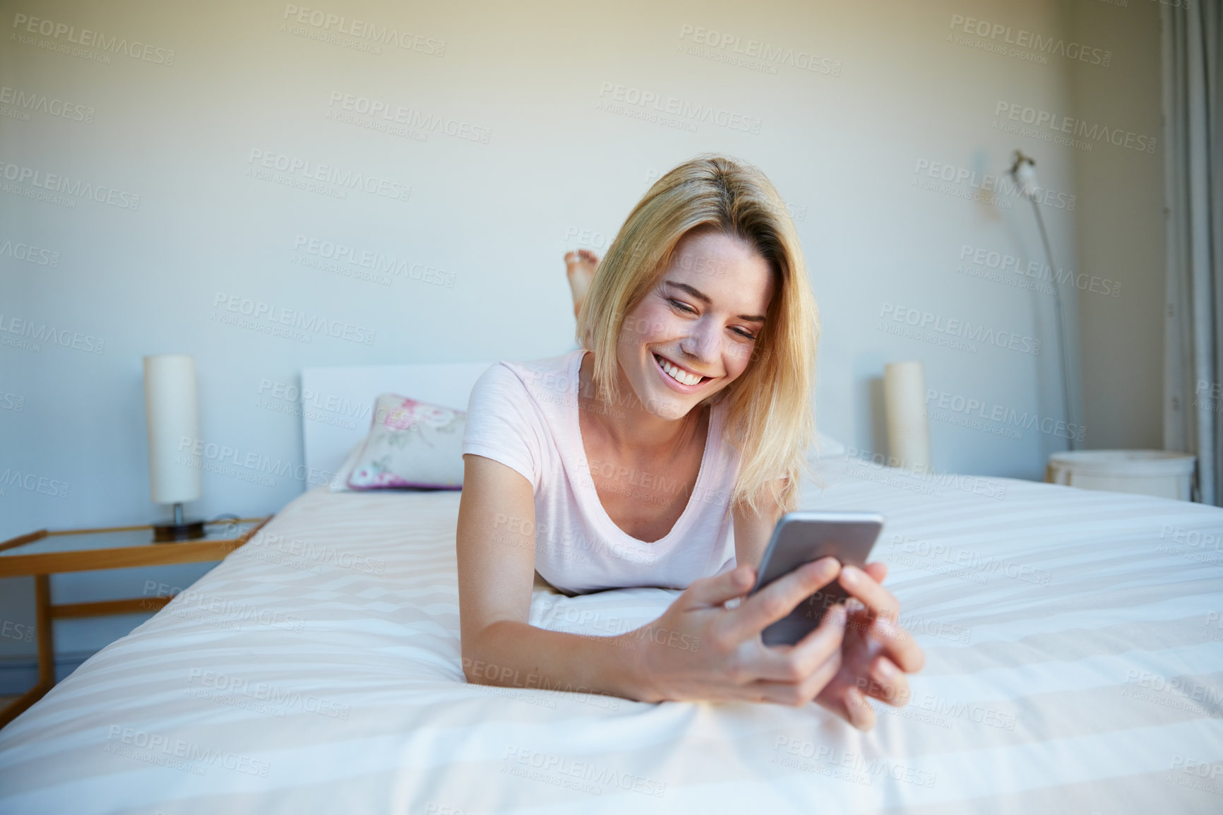 Buy stock photo Shot of a young woman using her cellphone while relaxing in her bedroom