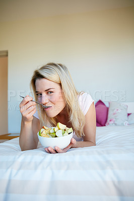 Buy stock photo Portrait shot of a young woman enjoying a fruit salad while relaxing in her bedroom