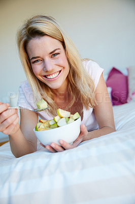 Buy stock photo Portrait shot of a young woman enjoying a fruit salad while relaxing in her bedroom