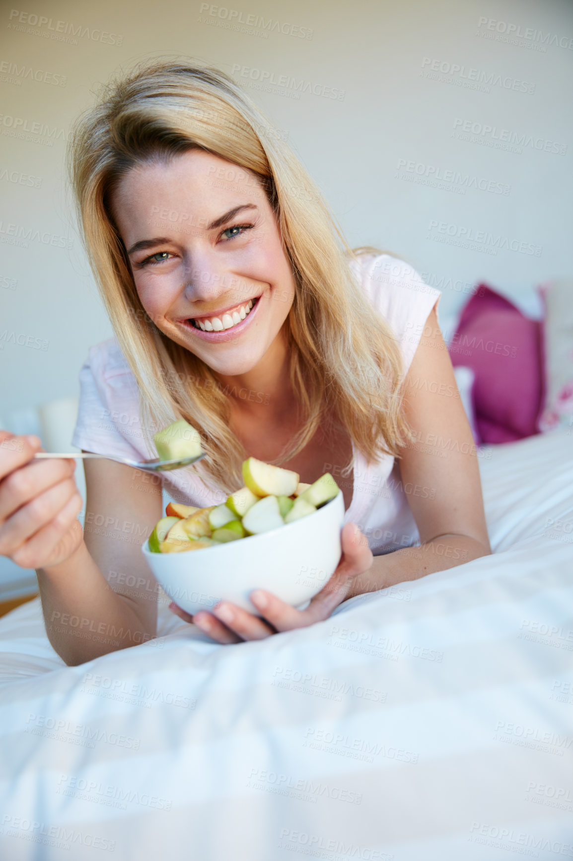 Buy stock photo Portrait shot of a young woman enjoying a fruit salad while relaxing in her bedroom