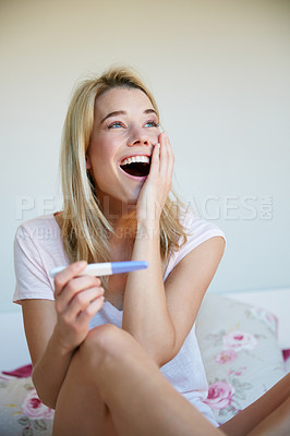 Buy stock photo A young blonde woman looking pleasantly surprised by the results of a pregnancy test