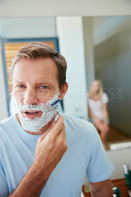 Buy stock photo Shot of a young man shaving his facial hair in the bathroom