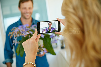 Buy stock photo Shot of a wife taking snapshots of her husband holding fresh flowers at home