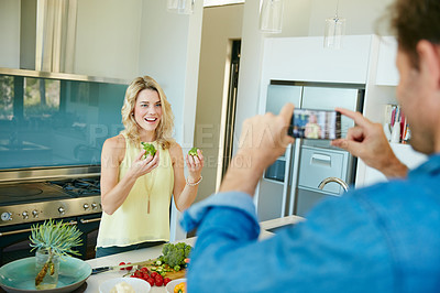 Buy stock photo Shot of a husband taking snapshots of his wife preparing a healthy meal at home