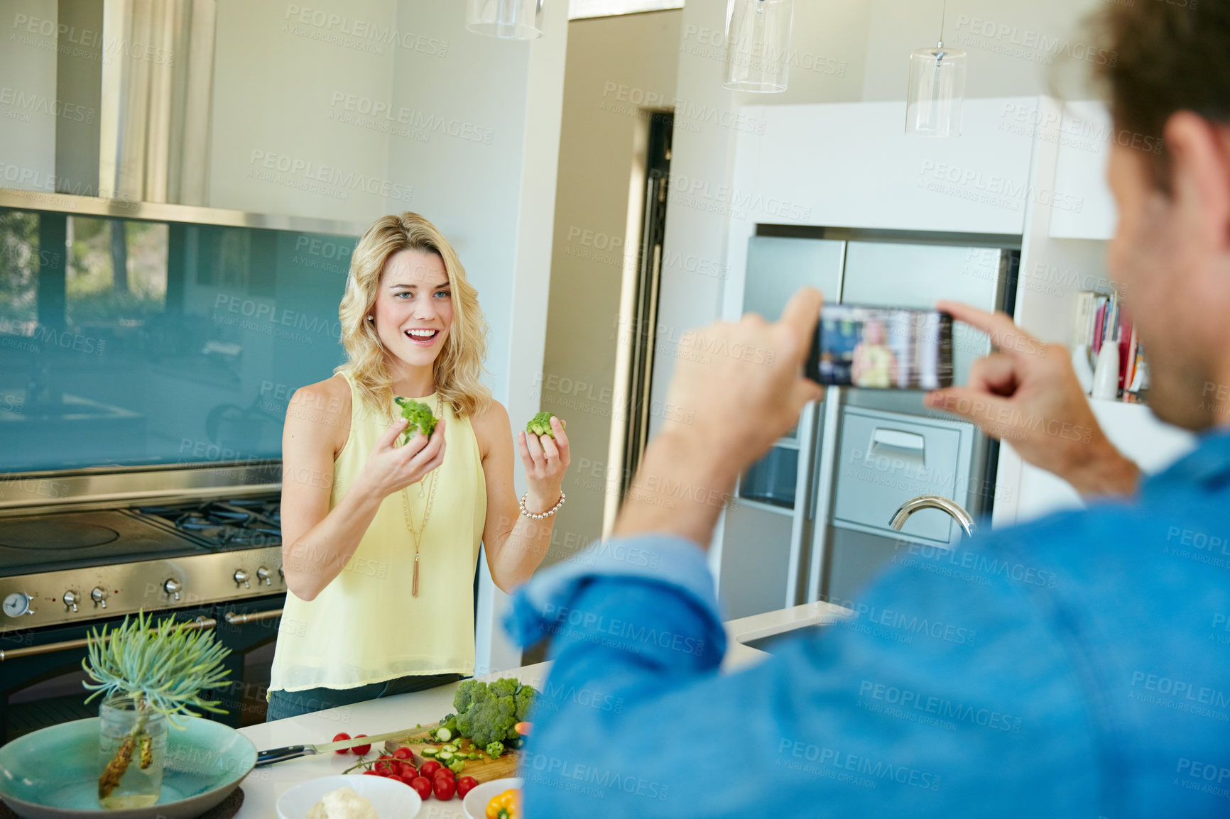 Buy stock photo Shot of a husband taking snapshots of his wife preparing a healthy meal at home