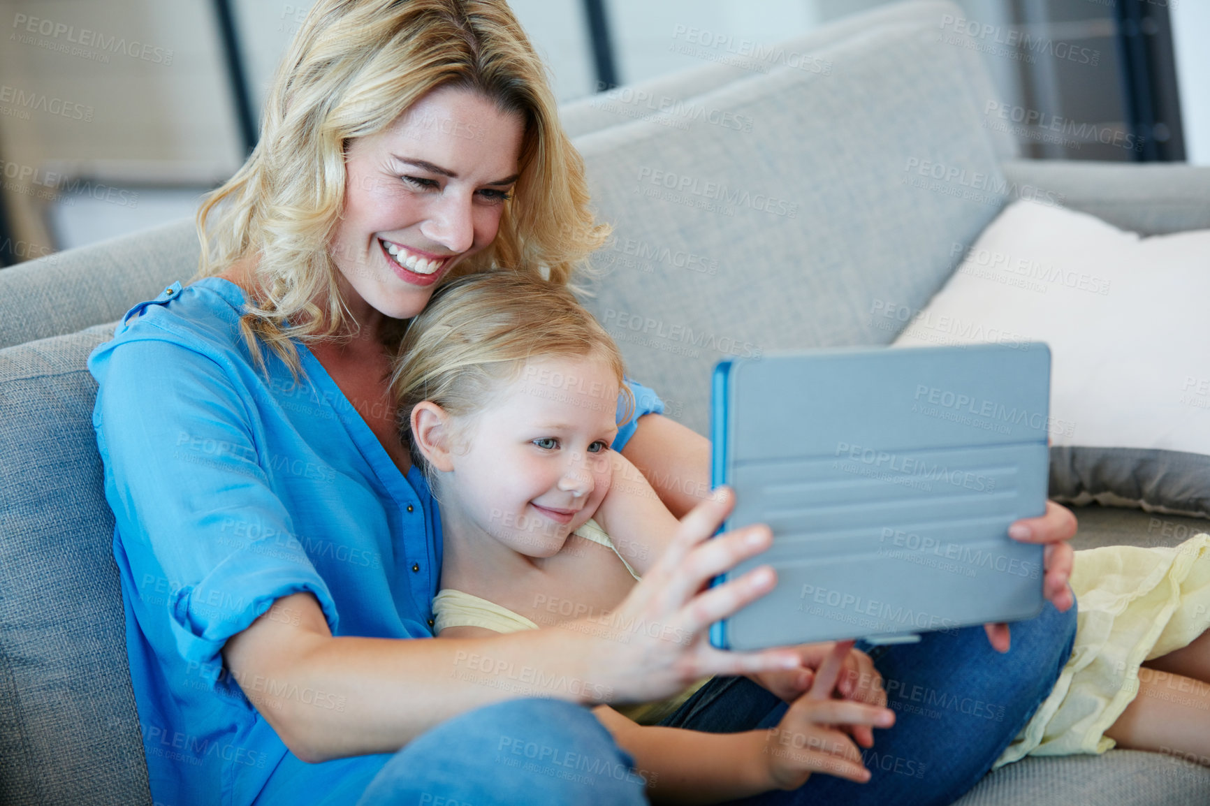 Buy stock photo Shot of a young mother and her daughter watching something on a tablet while sitting on the sofa at home