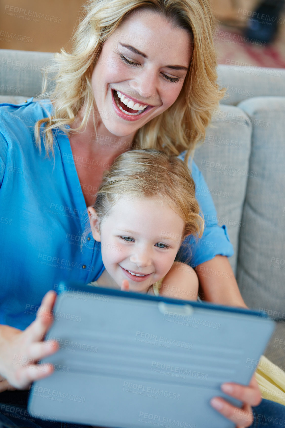 Buy stock photo Shot of a young mother and her daughter watching something on a tablet while sitting on the sofa at home