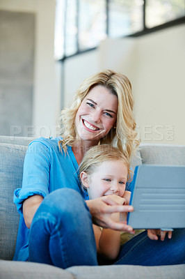 Buy stock photo Shot of a young mother and her daughter watching something on a tablet while sitting on the sofa at home