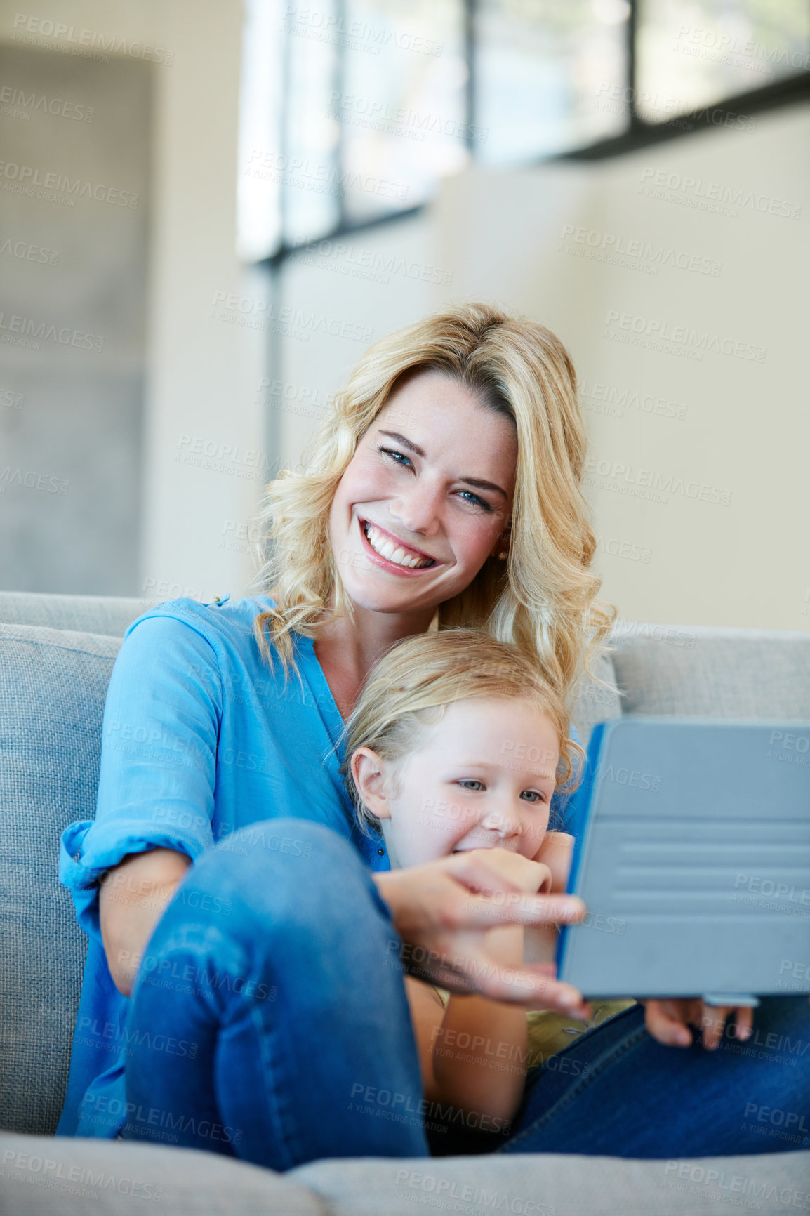 Buy stock photo Shot of a young mother and her daughter watching something on a tablet while sitting on the sofa at home