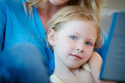 Buy stock photo Shot of a mother and her daughter watching something on a tablet while sitting on the sofa at home