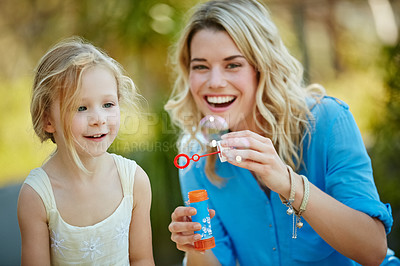 Buy stock photo Shot of a young mother and her daughter blowing bubbles outside