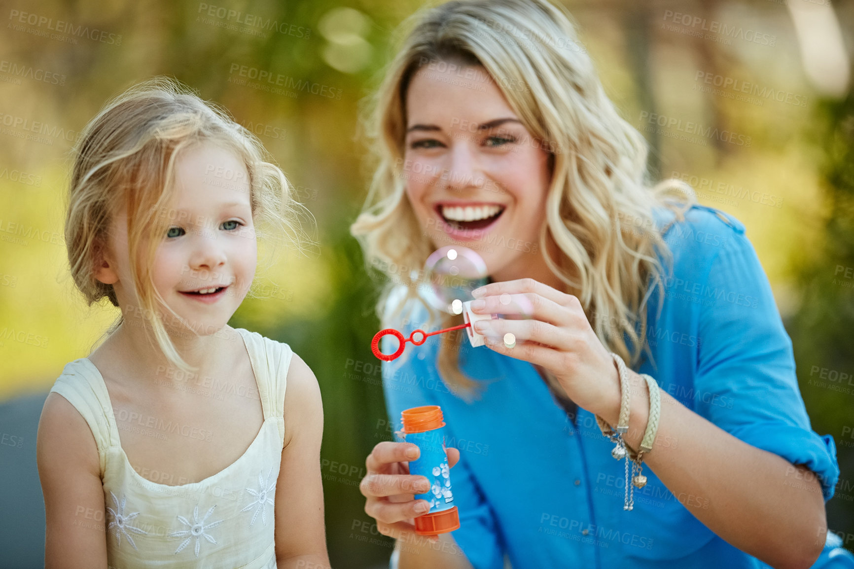 Buy stock photo Shot of a young mother and her daughter blowing bubbles outside