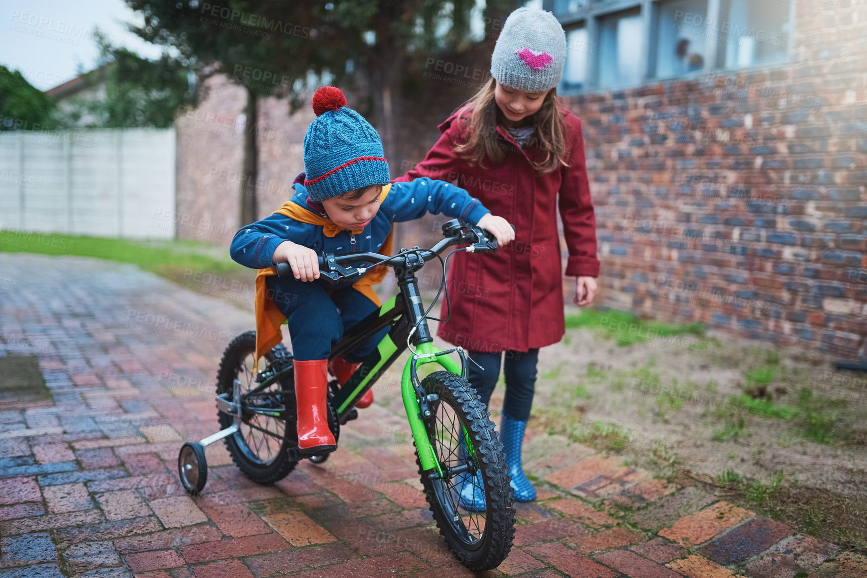 Buy stock photo Girl, siblings and teaching with bicycle for ride, training wheels or hobby in outdoor activity in neighborhood. Little child or kid helping young brother on bike for playful cycling or trip at park