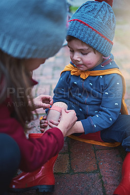Buy stock photo Cropped shot of a young girl putting a plaster on her little brother's knee