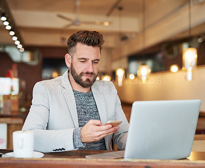 Buy stock photo Cropped shot of a modern businessman using his laptop and cellphone in a coffee shop