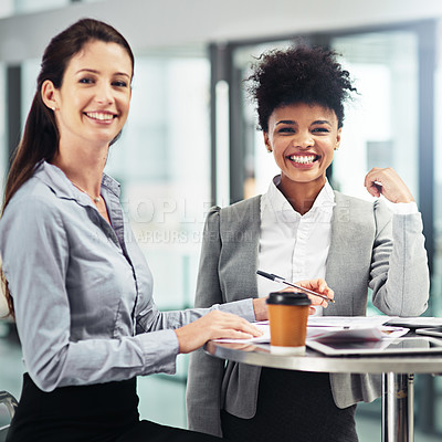 Buy stock photo Shot of two smiling businesswomen sitting together at a table in an office