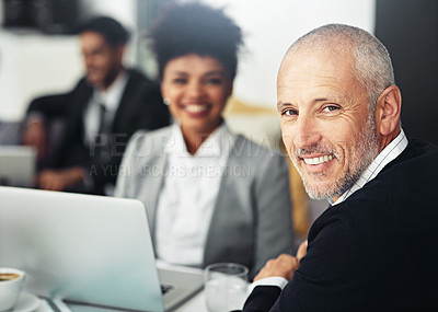Buy stock photo Portrait of a smiling mature businessman sitting in an office with colleagues in the background