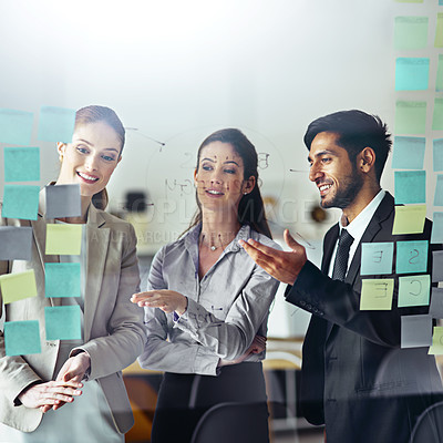 Buy stock photo Shot of a group of businesspeople brainstorming on a glass wall with sticky notes in an office