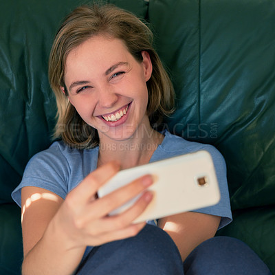 Buy stock photo Shot of a happy young woman taking a selfie with her smatphone at home