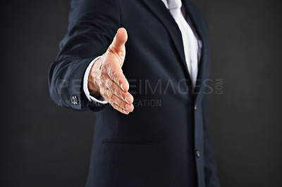 Buy stock photo Cropped shot of a businessman extending his arm to shake hands against a black background