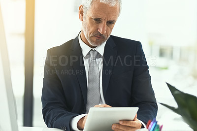 Buy stock photo Shot of a mature businessman using a digital tablet while sitting at his desk in an office