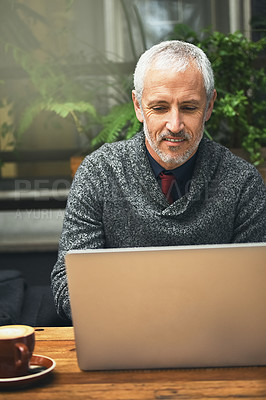 Buy stock photo Shot of a mature businessman using his laptop in a cafe