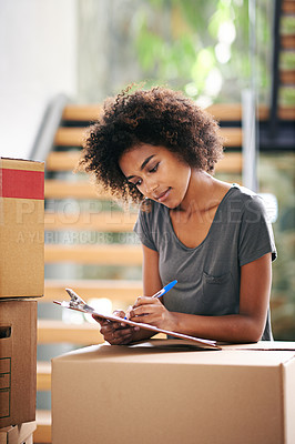 Buy stock photo Shot of a young woman checking her clipboard while busy packing up