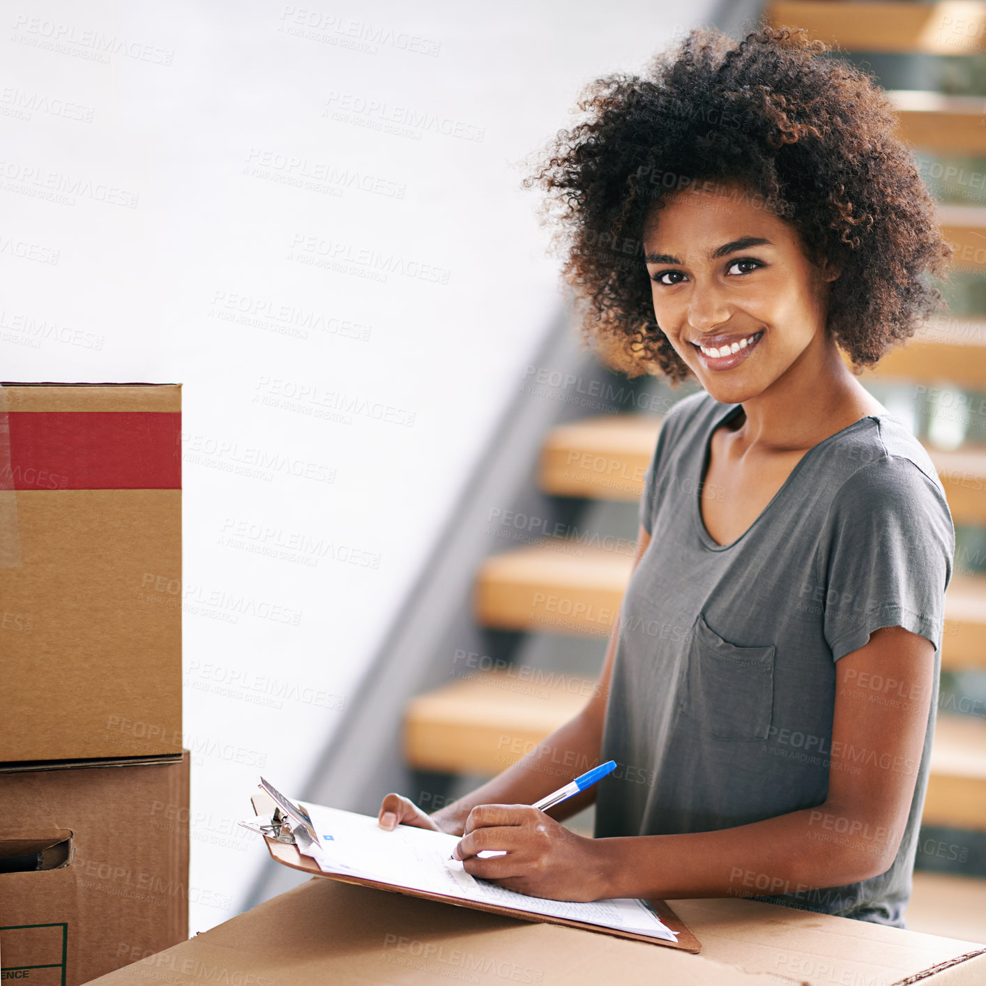 Buy stock photo Shot of a young woman checking her clipboard while busy packing up