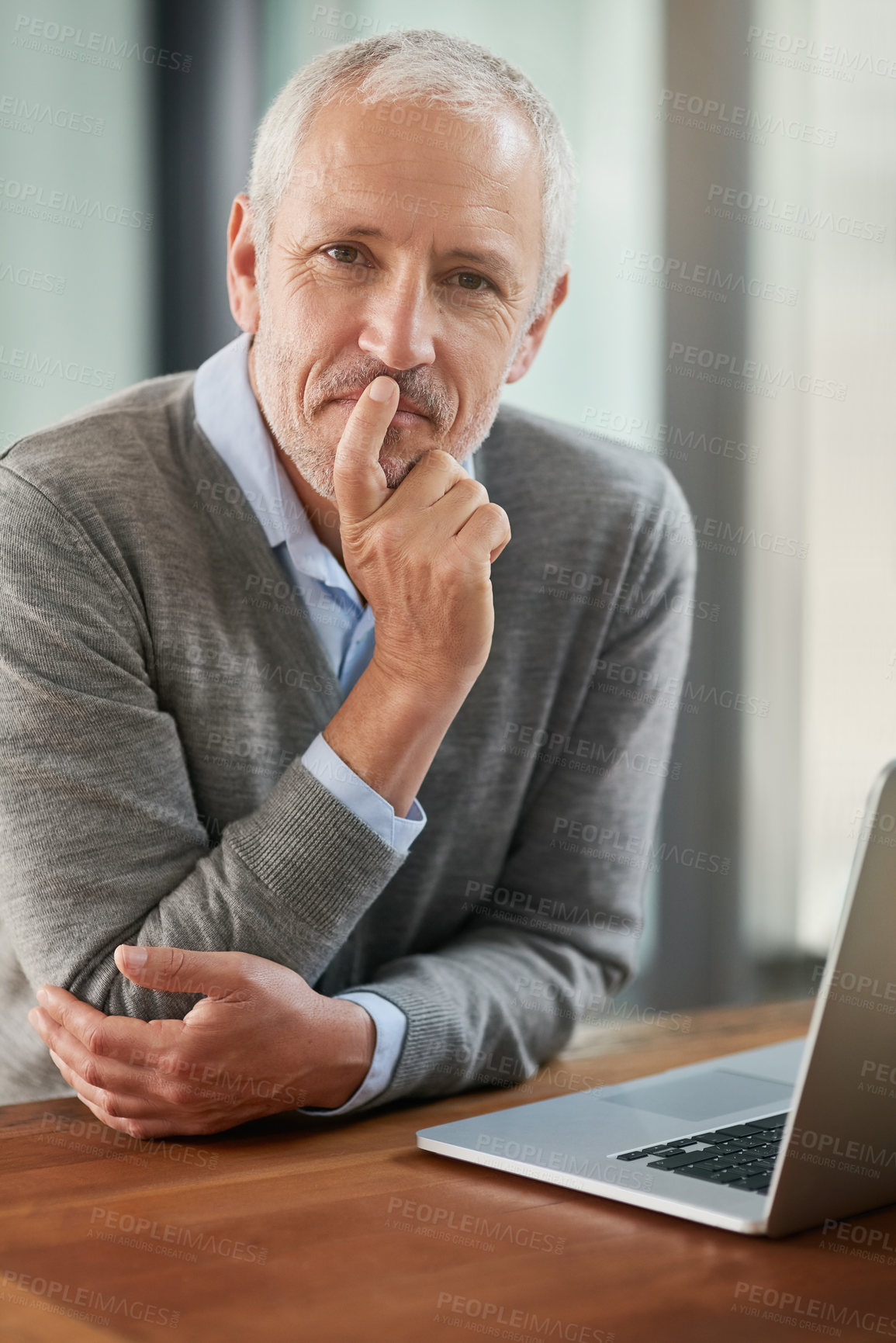 Buy stock photo Portrait of a mature businessman looking thoughtful while working on his laptop in the office