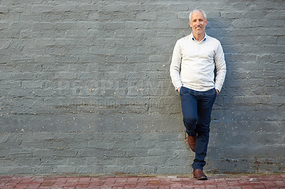Buy stock photo Portrait of a mature businessman standing with his hands in his pockets against a brick wall