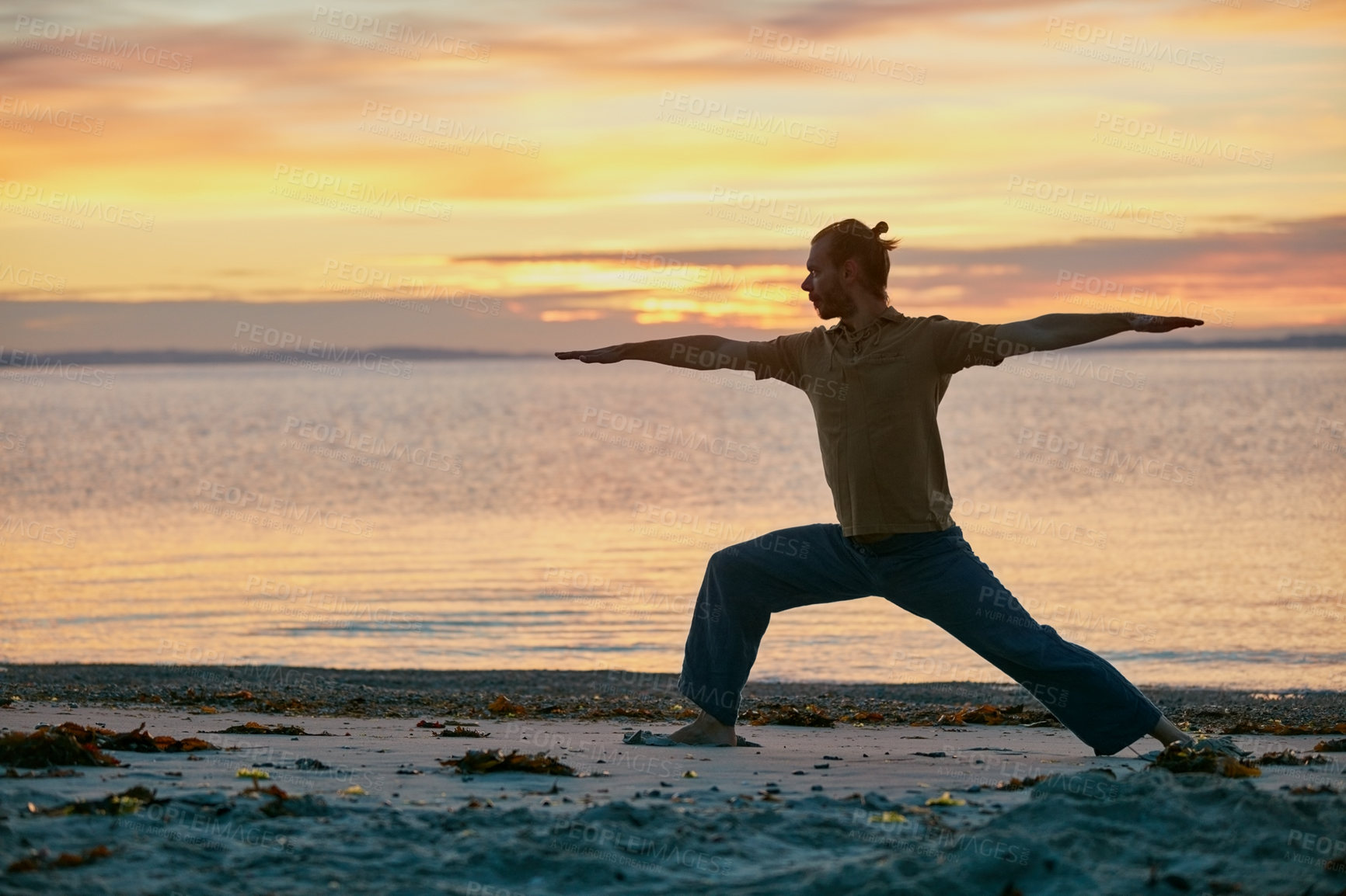 Buy stock photo Shot of a man practicing the warrior pose during his yoga routine at the beach