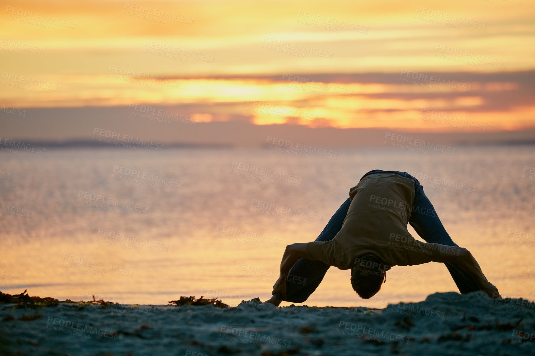 Buy stock photo Shot of a man practicing the wide legged forward bend during his yoga routine at the beach