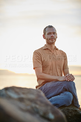 Buy stock photo Shot of a peaceful man sitting on a rock at the beach