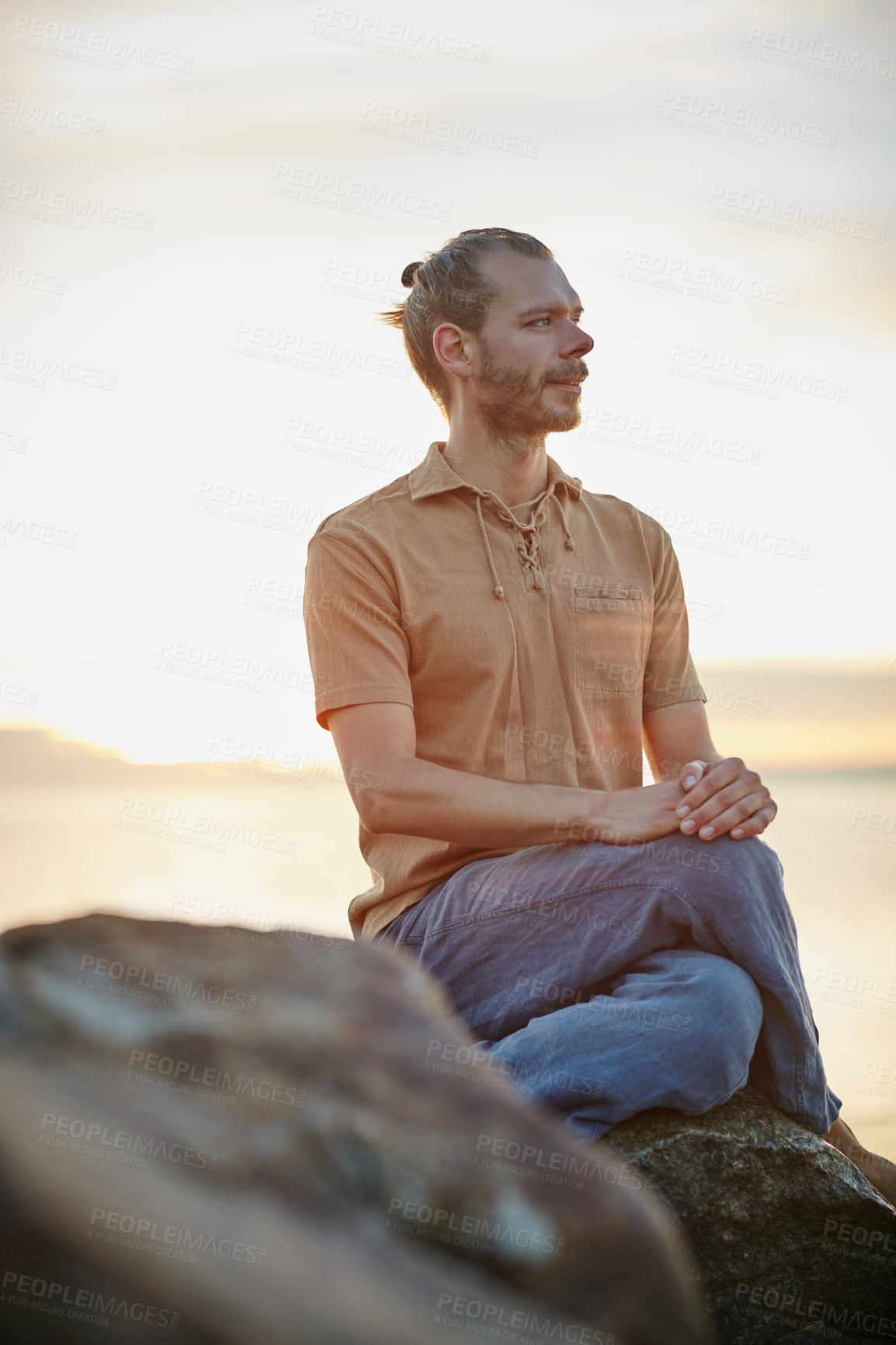 Buy stock photo Shot of a peaceful man sitting on a rock at the beach