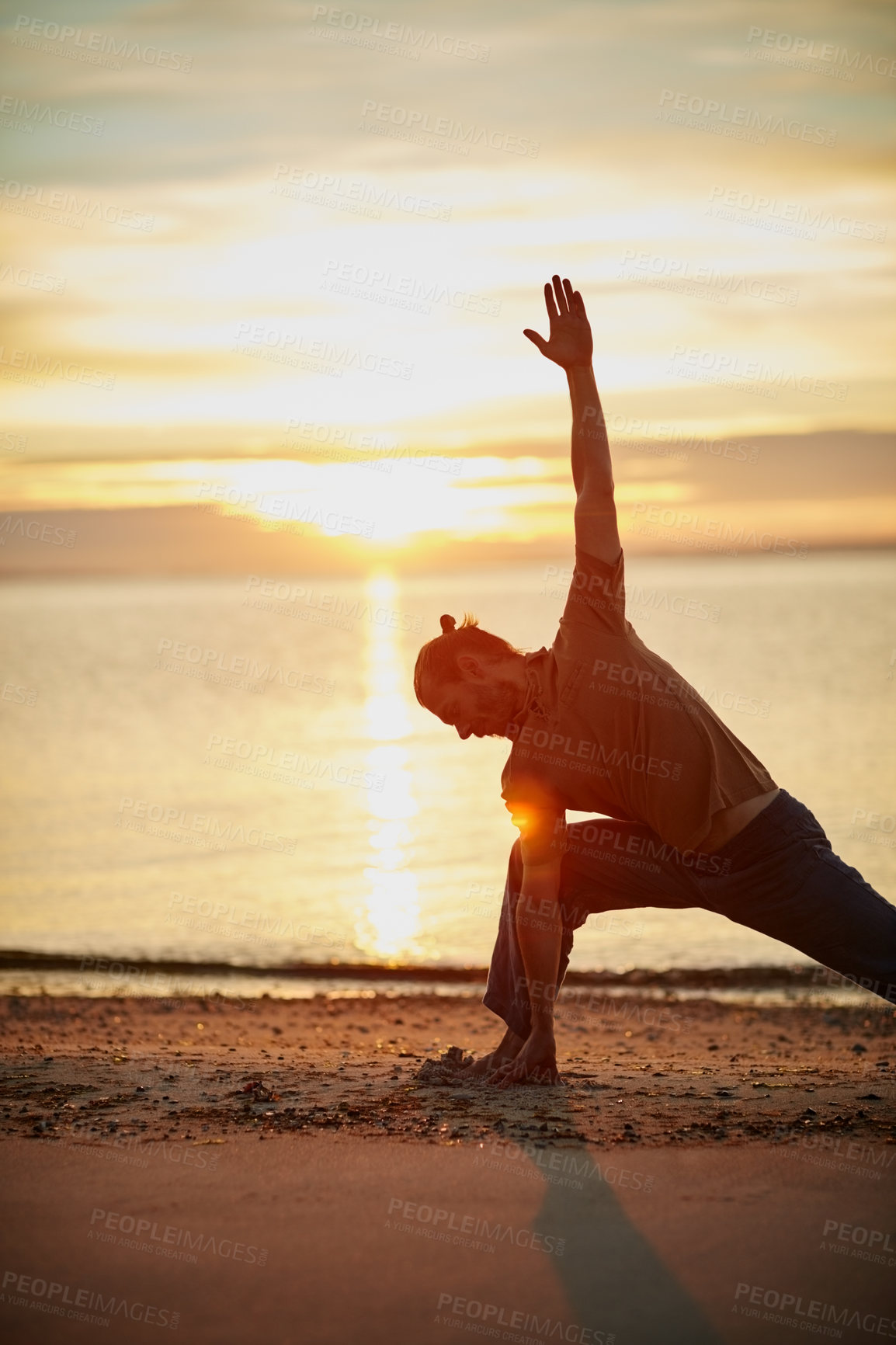 Buy stock photo Shot of a man practicing the triangle pose during his yoga routine at the beach