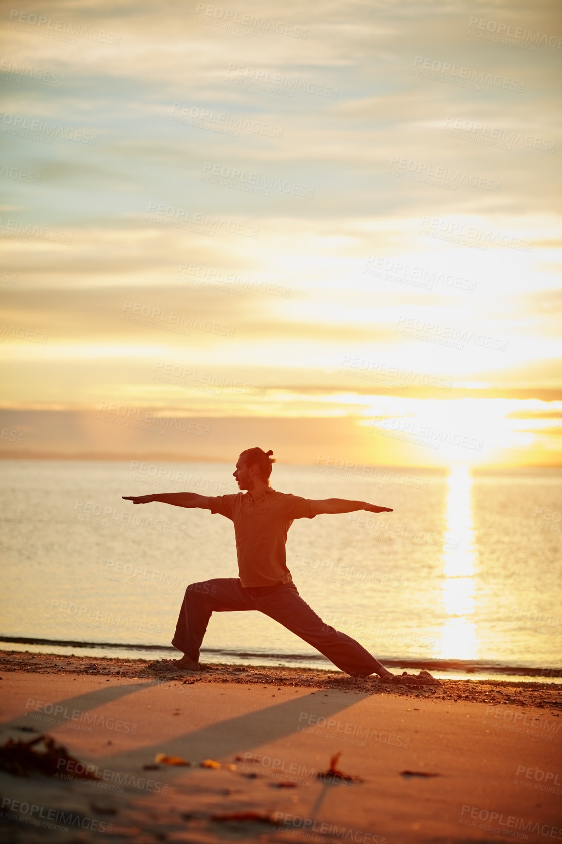 Buy stock photo Shot of a man practicing the warrior pose during his yoga routine at the beach