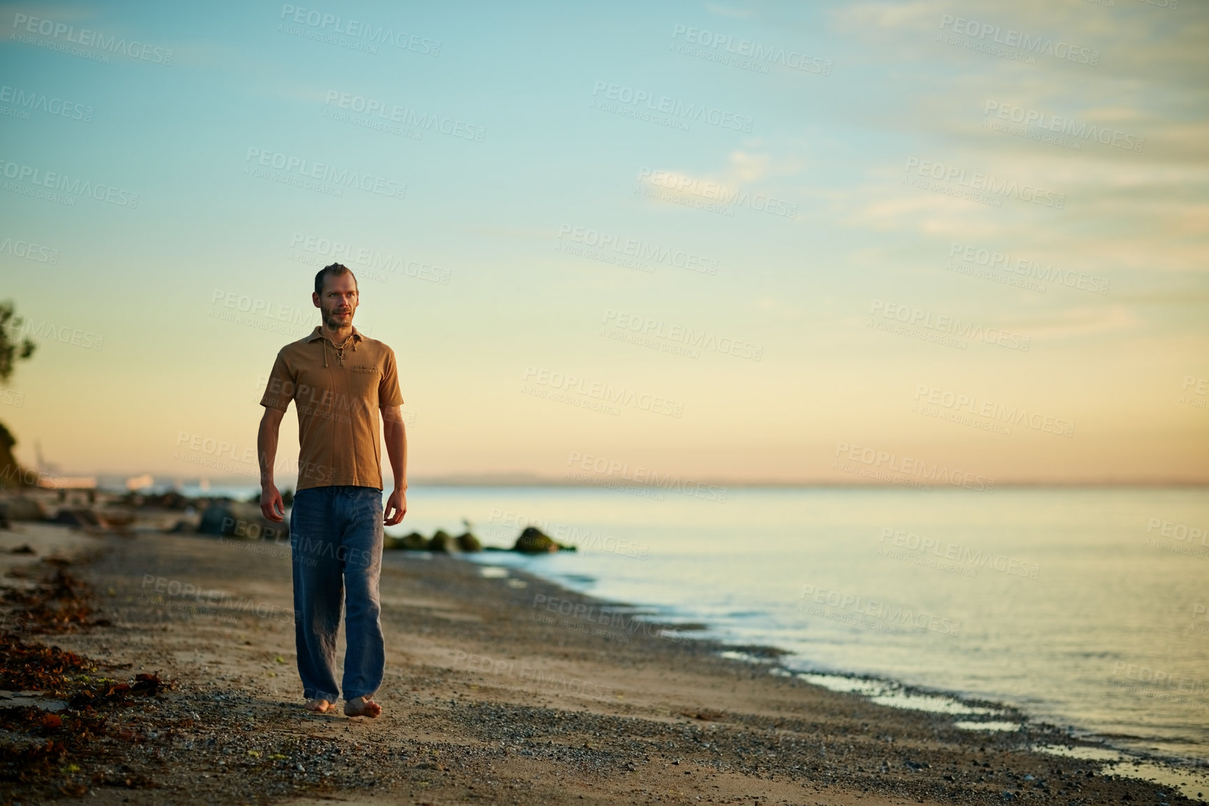 Buy stock photo Shot of a man going for a walk along the water’s edge at the beach