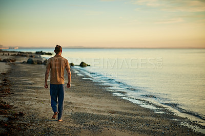 Buy stock photo Rearview shot of a man going for a walk along the water’s edge at the beach