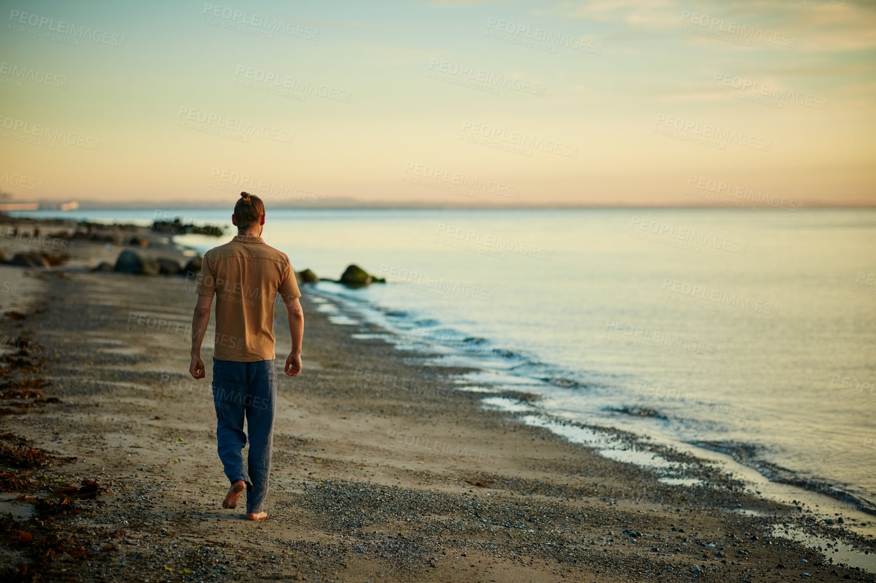 Buy stock photo Rearview shot of a man going for a walk along the water’s edge at the beach