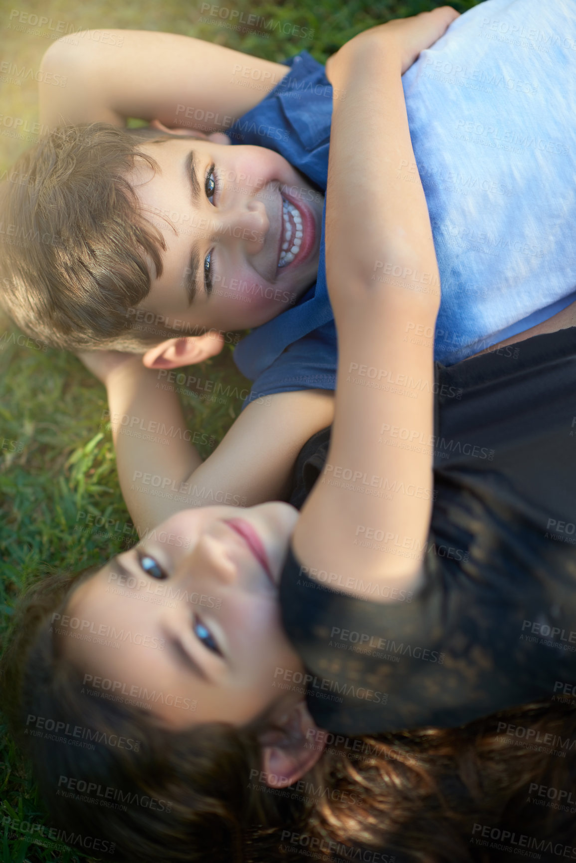 Buy stock photo Portrait of a pair of young siblings hugging each other while lying on the grass outside their home