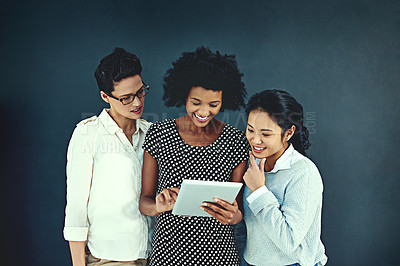 Buy stock photo Shot of a young businesswoman showing her colleagues something on a tablet in the studio